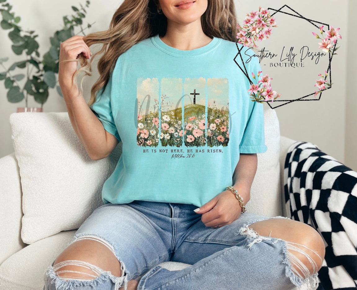 Christian He Is Risen t-shirt – Comfort Colors Easter faith-based graphic tee with Matthew 28:6 Bible verse and floral cross design.